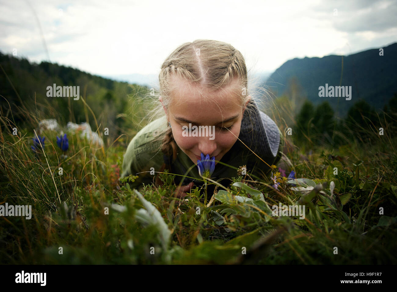 Caucasian girl smelling wildflower laying in grass sur hill Banque D'Images