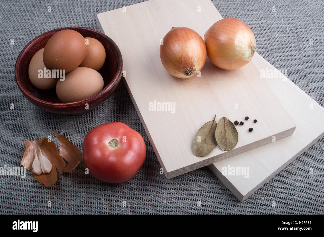 Ingrédients pour la cuisson des aliments dans vintage style - L'oeuf, l'oignon, la tomate, l'ail et les épices, des planches et une tasse sur fond textile Banque D'Images