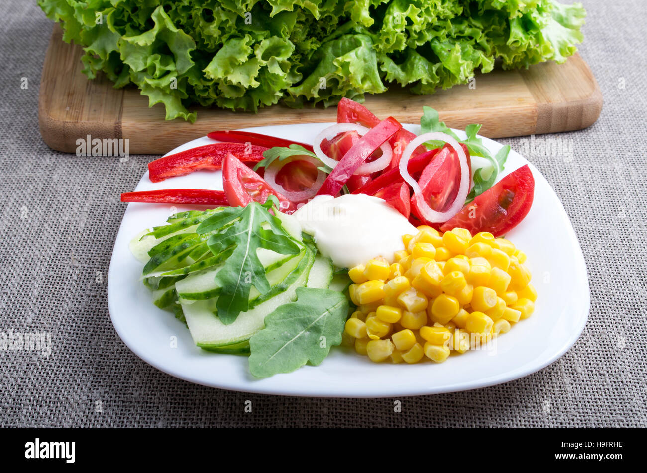 Un plat sain à base de tomates, poivrons, mozzarella bell-fromage, concombres, maïs, la laitue et la salade ruccola sur fond de nappe gris Banque D'Images