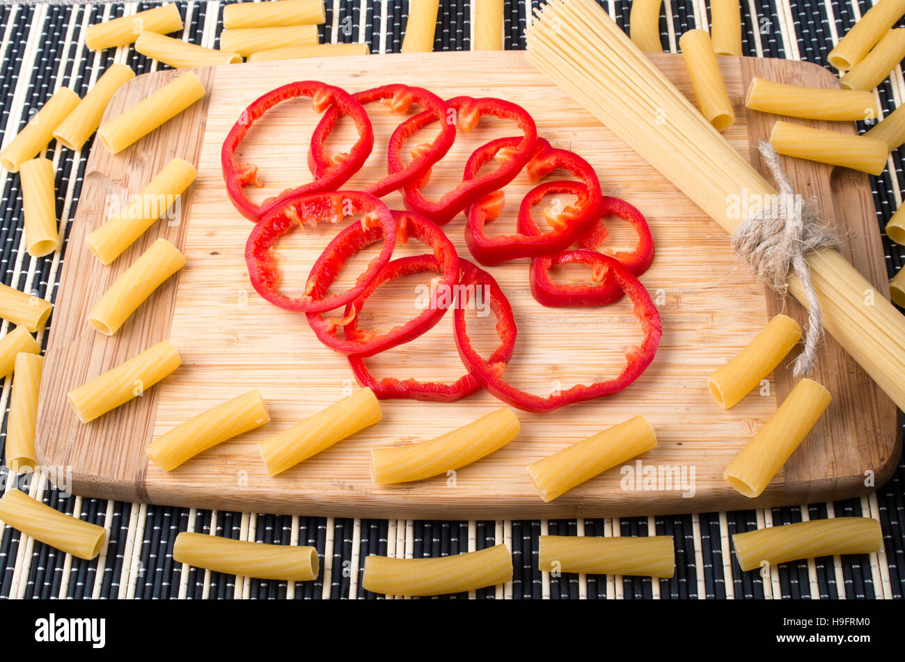 Ingrédients pour la cuisson sur la table de cuisine - pâtes italiennes et tranches de poivron rouge sur une planche en bois Banque D'Images