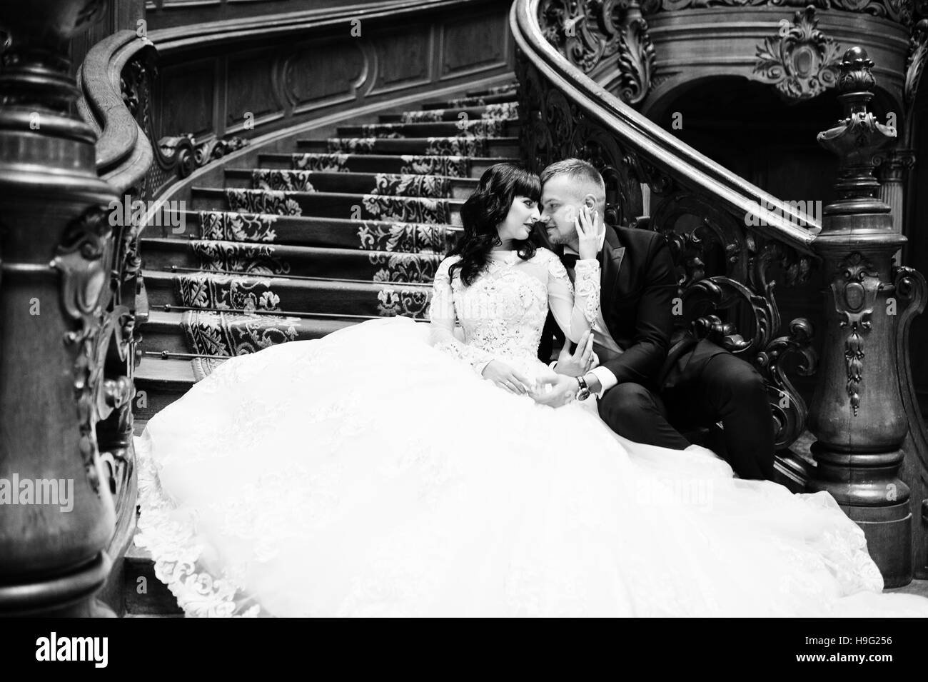 Charmant couple de mariés assis sur un escalier en bois riche sur grand palais royal. Banque D'Images