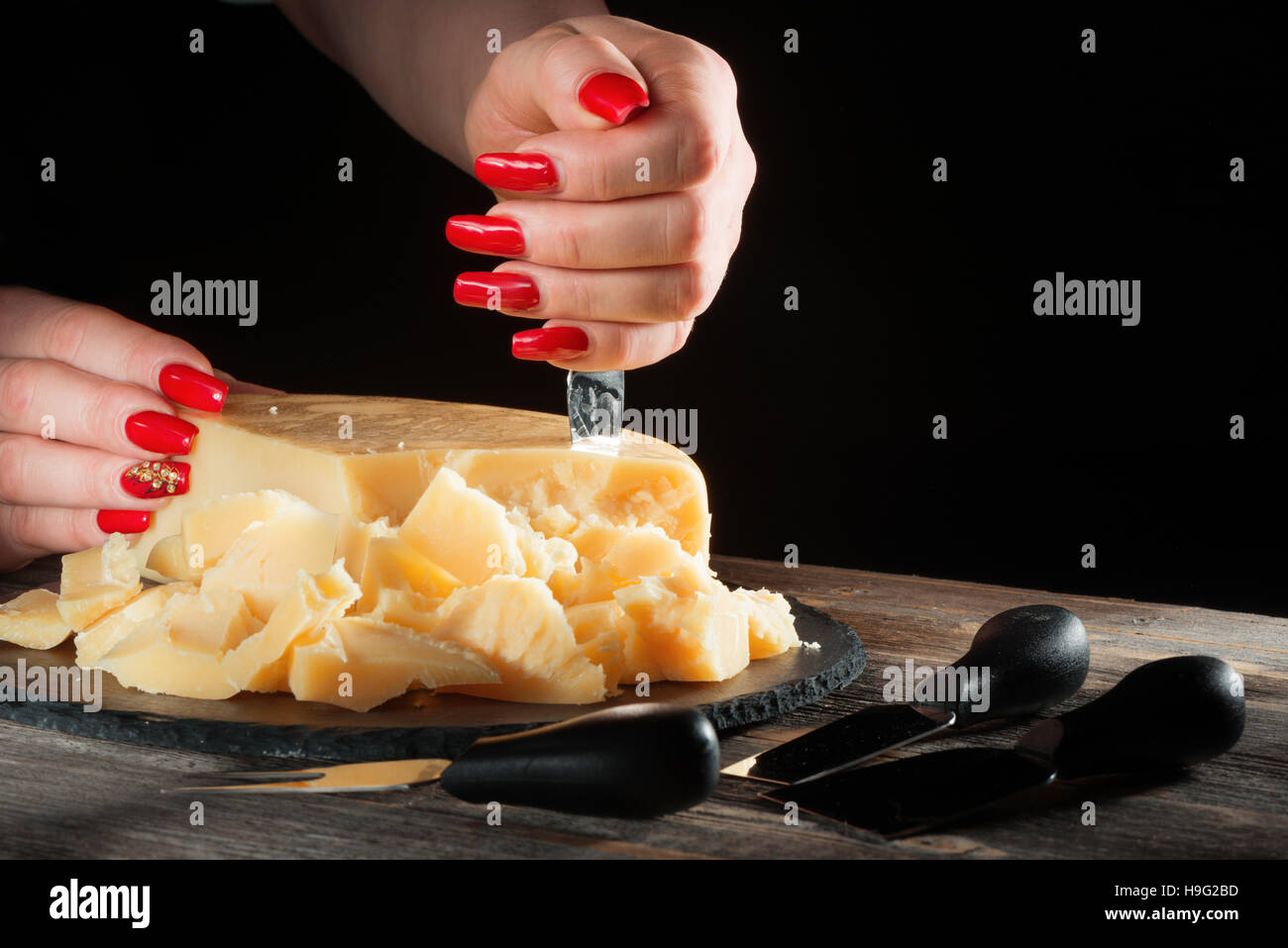 Femmes avec des belles manucure rompre des morceaux de fromage à pâte dure comme le parmesan à l'aide d'un couteau spécial Banque D'Images