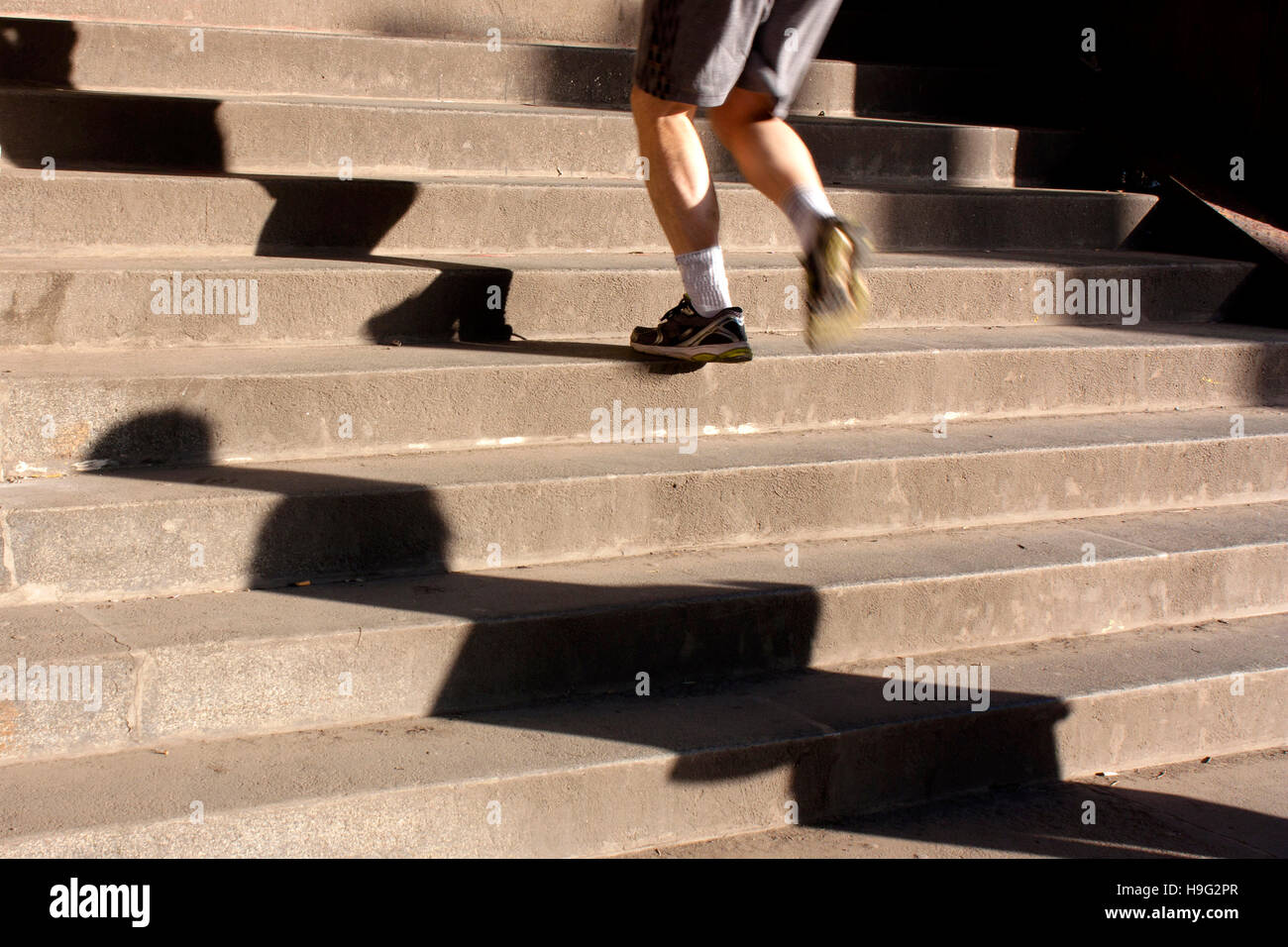 Les jambes d'un homme en short et baskets courir vers le haut des escaliers de la ville et de grandes ombres. Motion Blur Banque D'Images