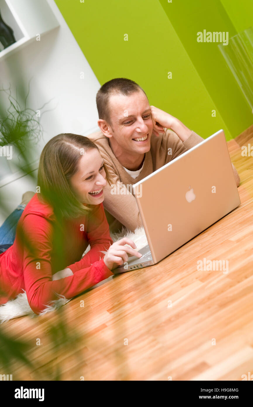 Couple allongé sur le plancher du salon, travailler sur un ordinateur portable Banque D'Images