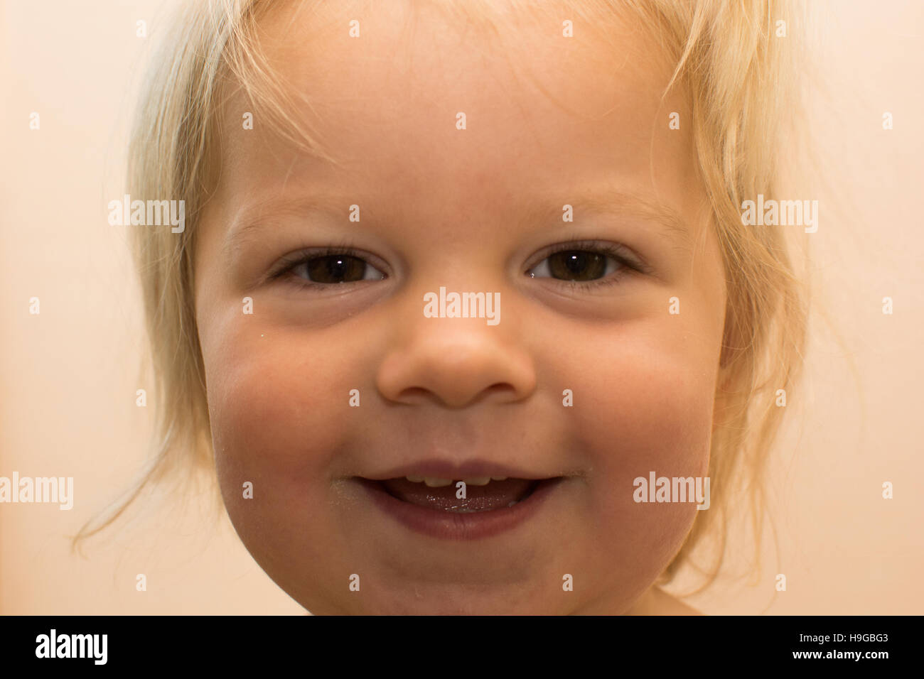 1 ans fille blonde à la recherche directement dans Appareil photo avec sourire malicieux et les yeux bruns Banque D'Images