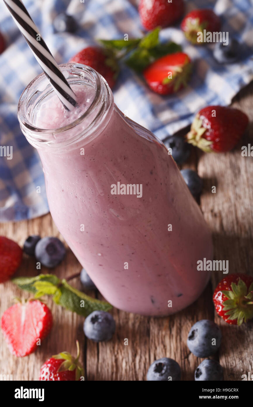 Smoothie lait délicieux avec des fraises et des bleuets dans une bouteille en verre sur la table verticale. Banque D'Images