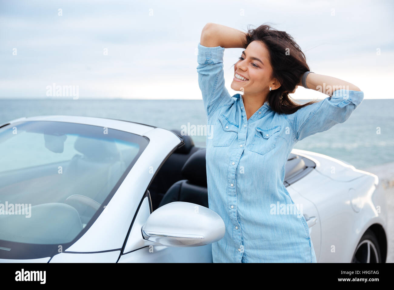 Jeune brunette femme debout à côté de sa nouvelle voiture au bord de la mer Banque D'Images