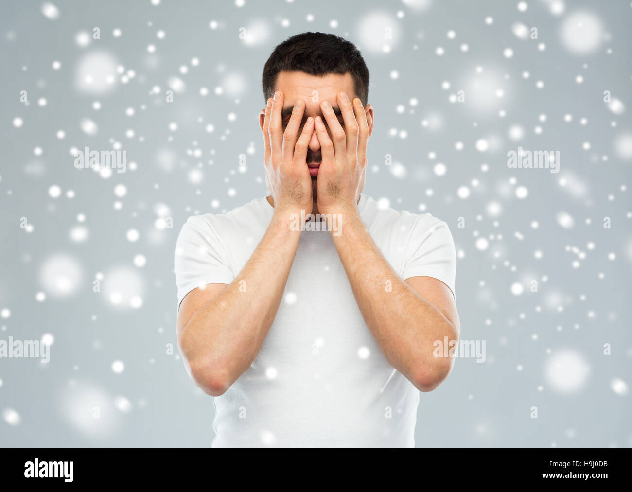 Homme couvrant son visage avec les mains sur la neige Banque D'Images