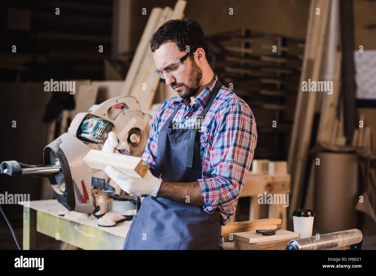 Beau Carpenter dans des lunettes, debout près de son objet en bois dans l'atelier Banque D'Images