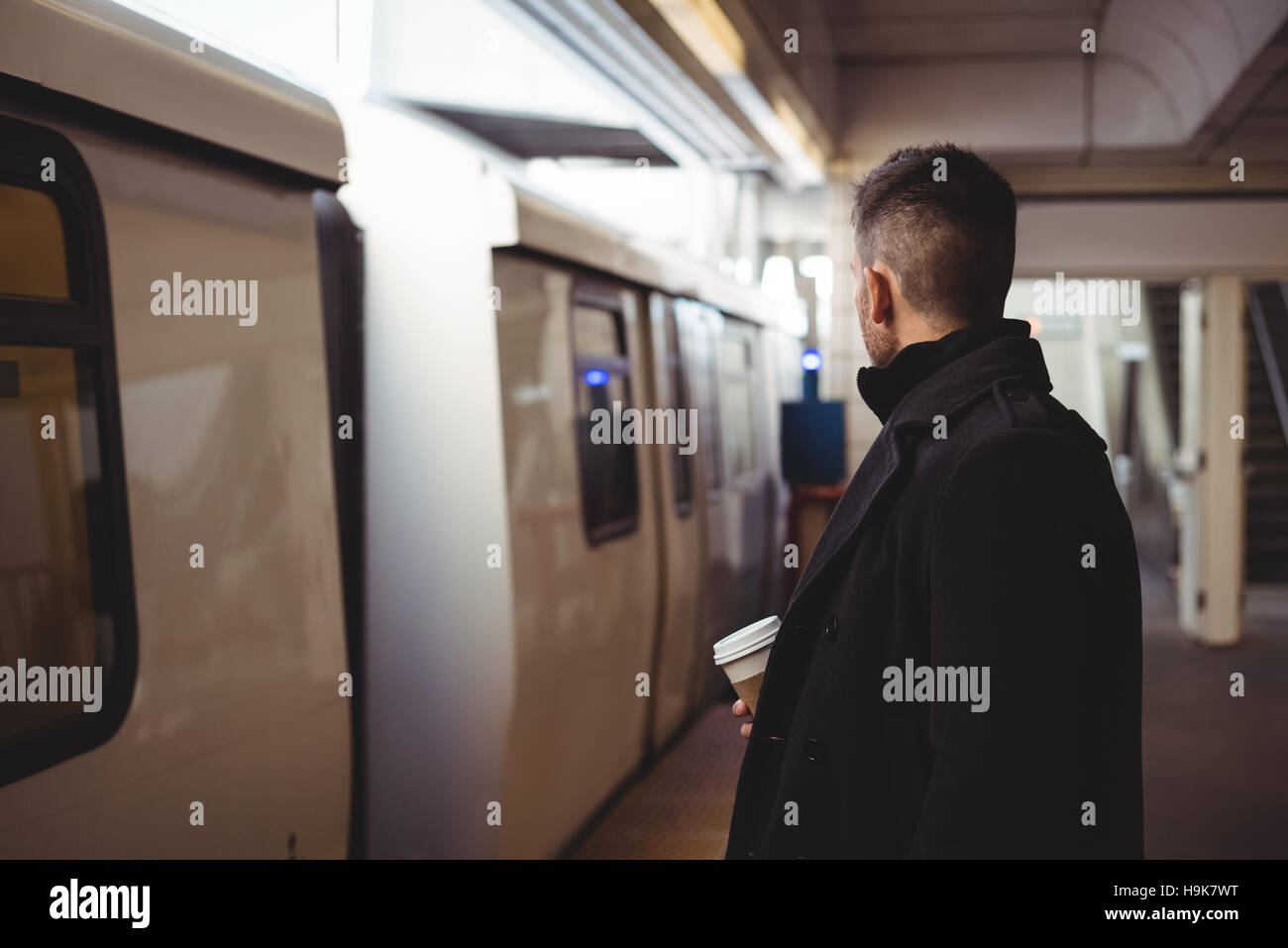 Avec un homme d'une tasse à café jetable en attente de train Banque D'Images