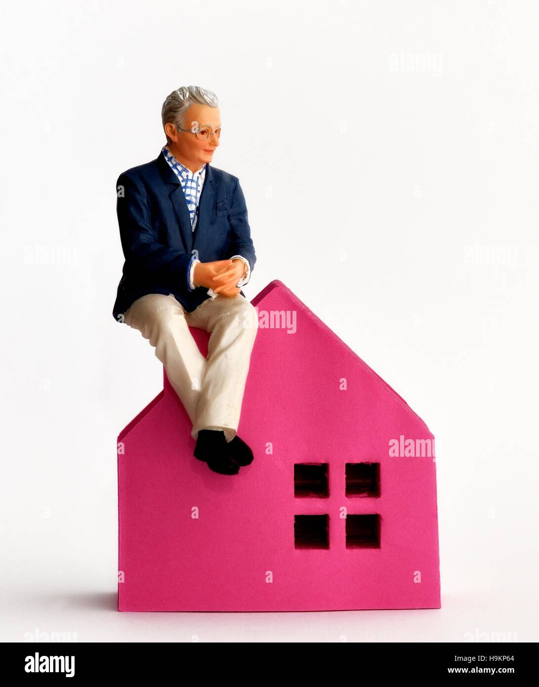 Une vieille figurine senior homme assis sur une maison rose. Banque D'Images