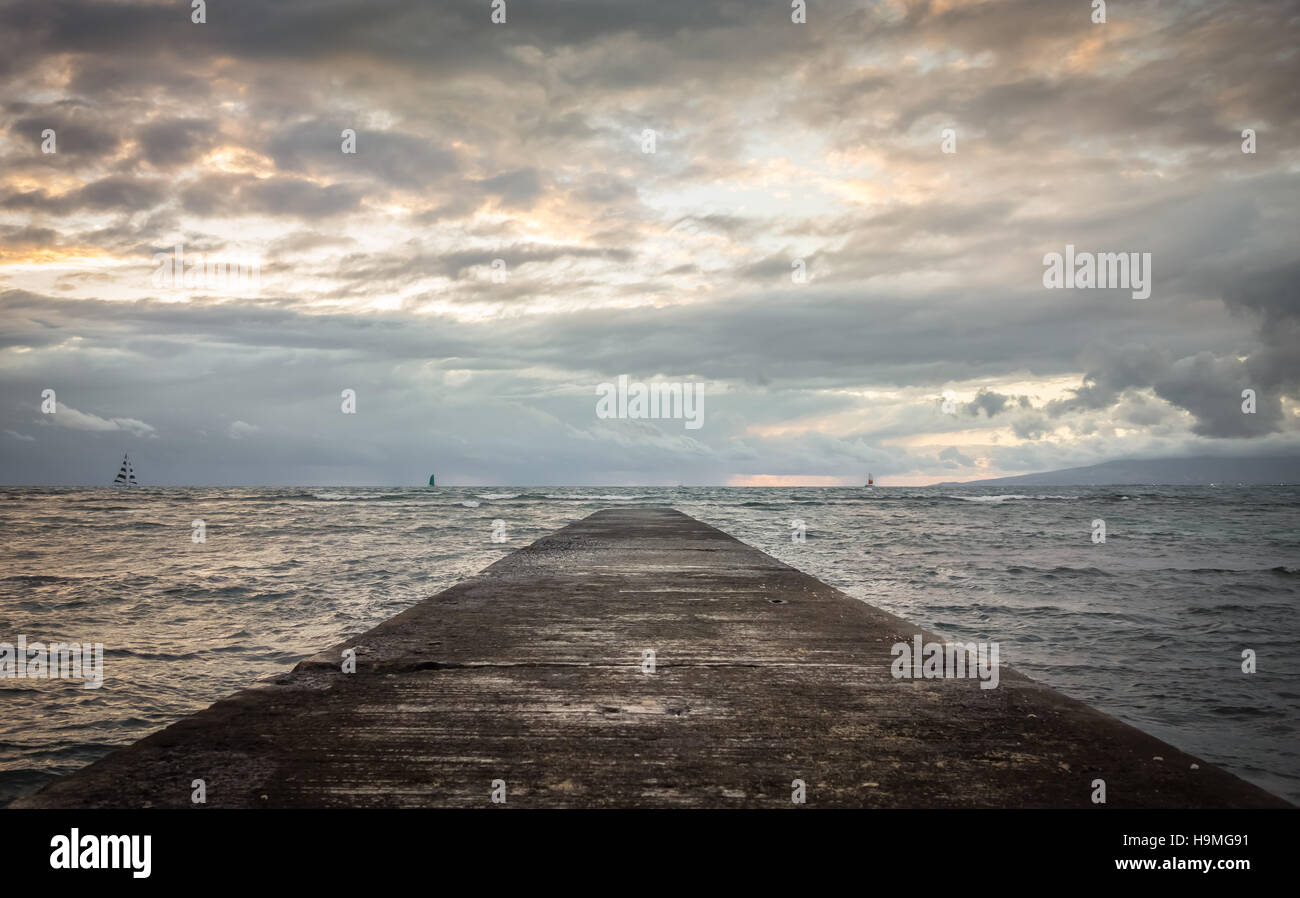 Jetée de Waikiki en tendant vers l'océan où les bateaux de croisière le long de la voile nuageux soir horizon. Banque D'Images