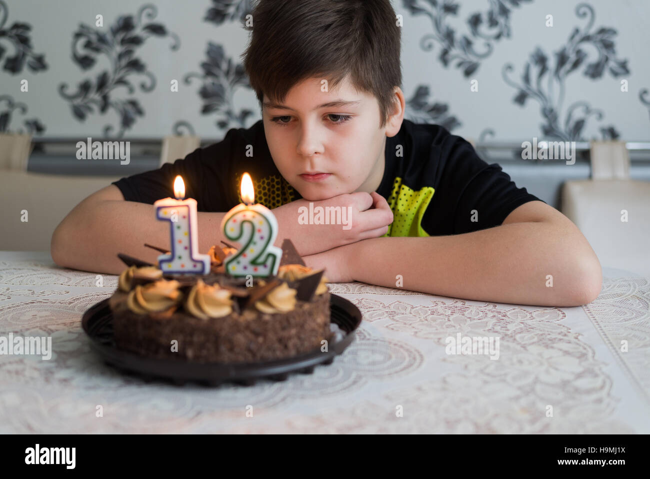 Teen boy regarde pensivement au gâteau avec des bougies sur le douzième jour de naissance Banque D'Images