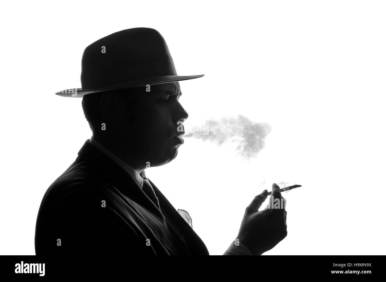 Silhouette de détective privé s'allume cigarette. Agent recherche comme Al Capone rester côté à huis clos. Scène criminelle de police en noir et blanc. Gangster studio shot Banque D'Images Silhouette de détective privé s'allume cigarette. Agent recherche comme Al Capone rester côté à huis clos. Scène criminelle de police en noir et blanc. Gangster studio shot Banque D'Images