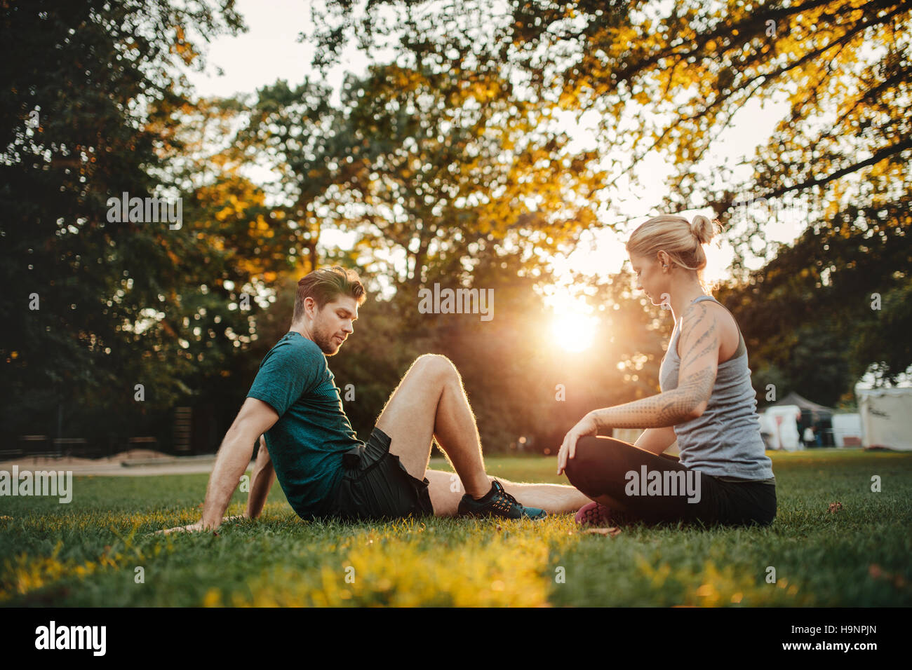 Shot of young couple sitting at park et l'élaboration. L'homme et de la femme de l'exercice à park de matin. Banque D'Images