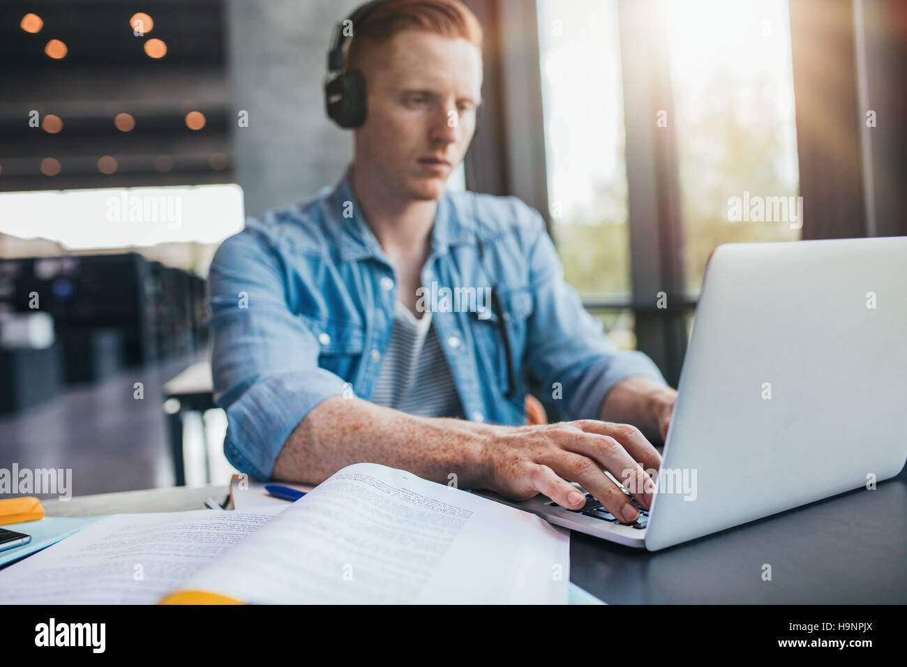 Male student in University Library à l'aide d'ordinateur portable. Jeune homme l'étude sur l'affectation de l'école. Banque D'Images