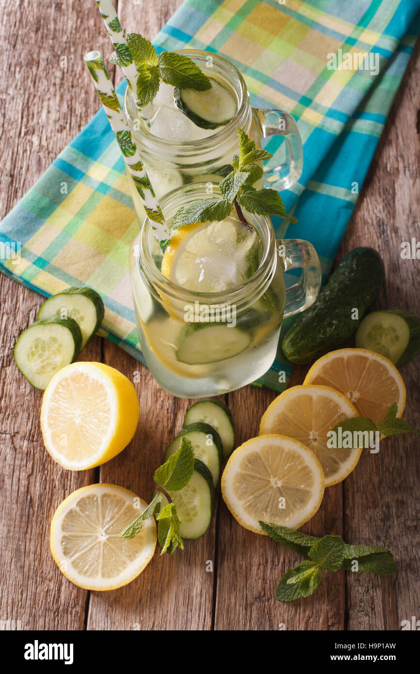 L'eau froide avec le concombre, le citron, la glace et la menthe close up dans un bocal en verre sur la table. vertical Vue de dessus Banque D'Images