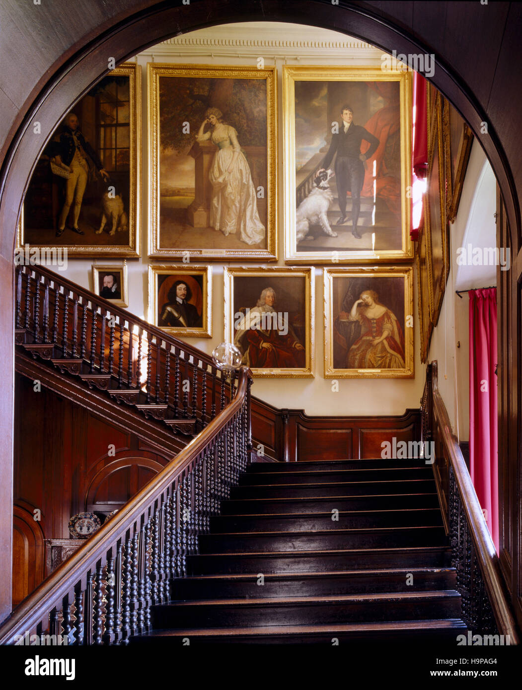 Hall d'entrée à Antony House montrant l'escalier avec balustrade en chêne , portraits, et arch. Banque D'Images