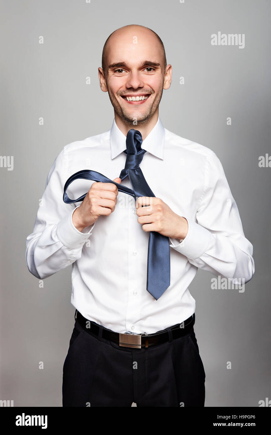 Studio shot of young smiling businessman tying une cravate. Portrait sur fond gris. Banque D'Images