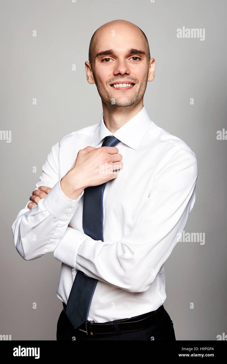 Jeune homme en chemise blanche fixant sa cravate. Studio shot sur fond gris. Banque D'Images