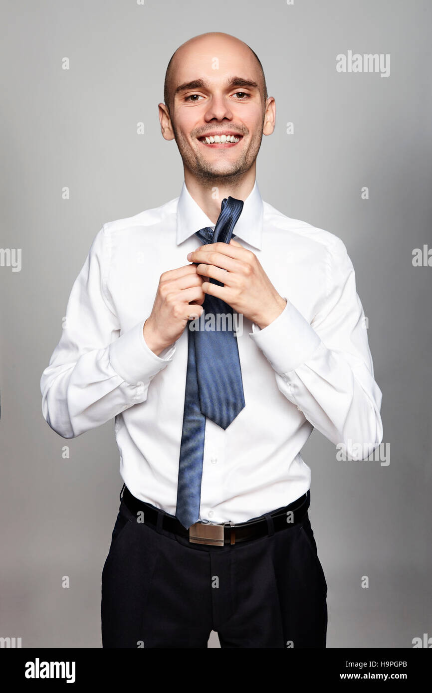 Portrait de jeune homme attachant une cravate. Portrait sur fond gris. Banque D'Images