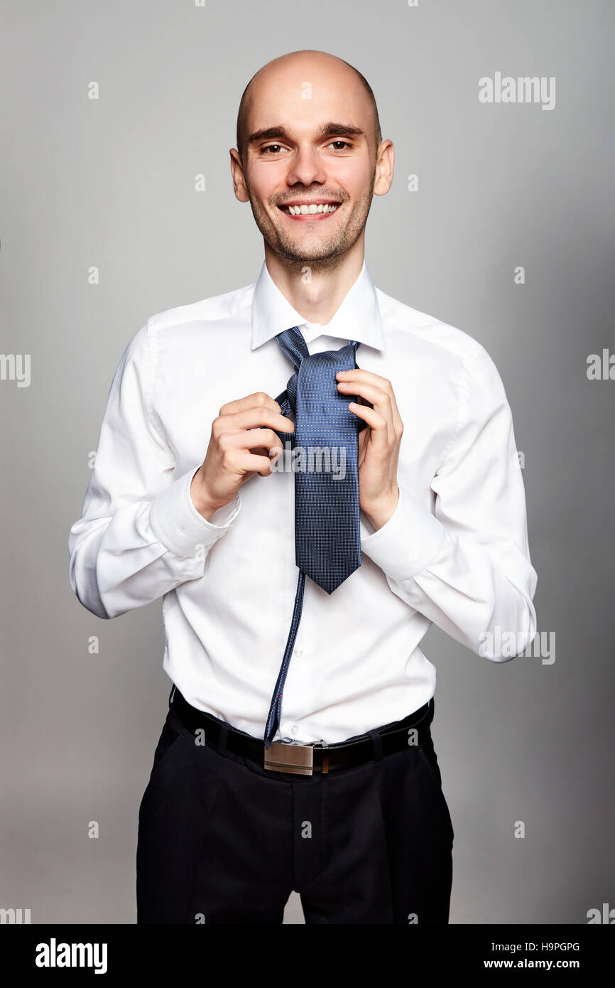 Studio shot of young smiling businessman tying une cravate. Portrait sur fond gris. Banque D'Images