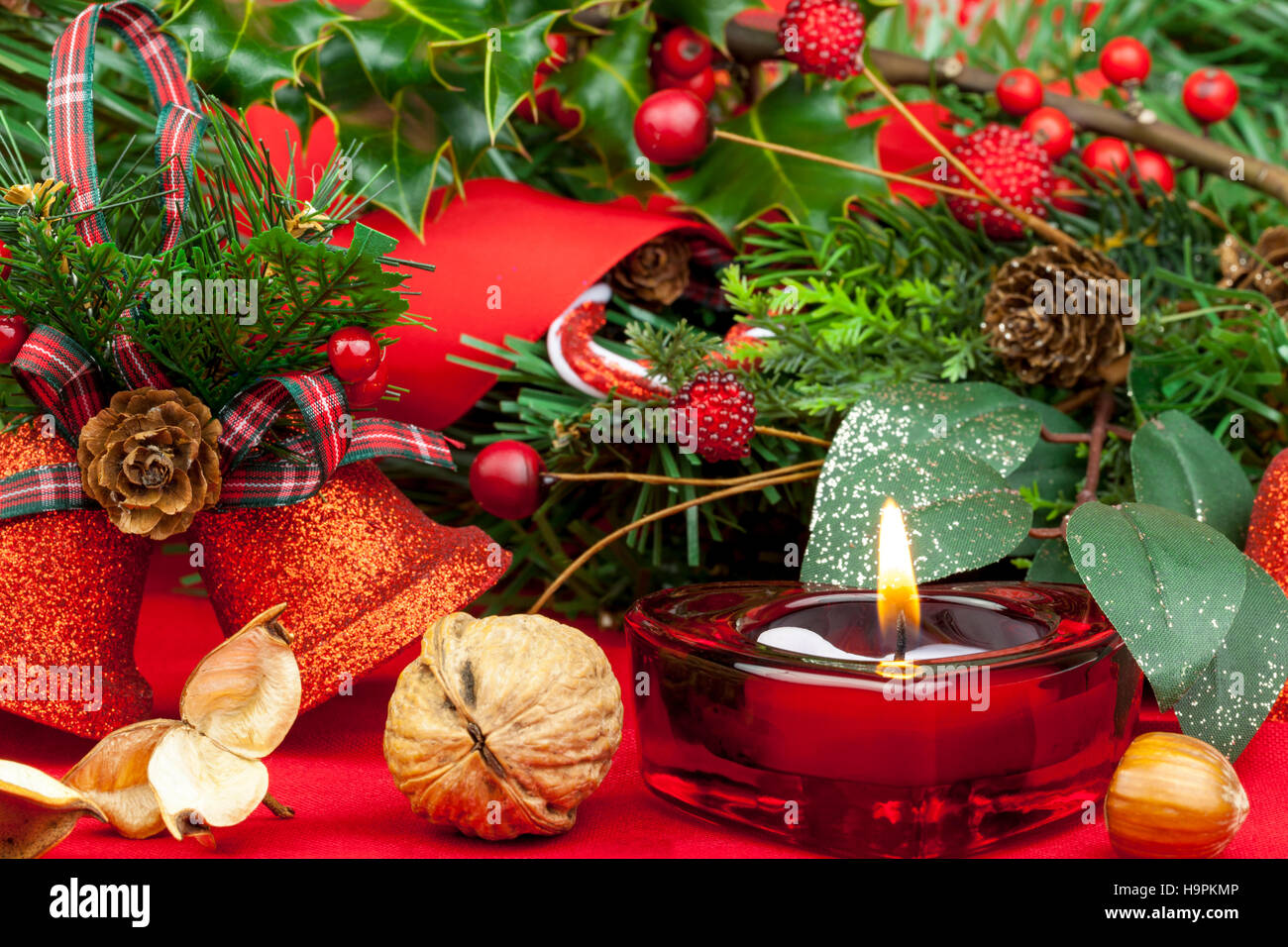 Red Heart shaped candle burning sur une table décorée pour Noël avec des cloches, des baies et Holly Banque D'Images
