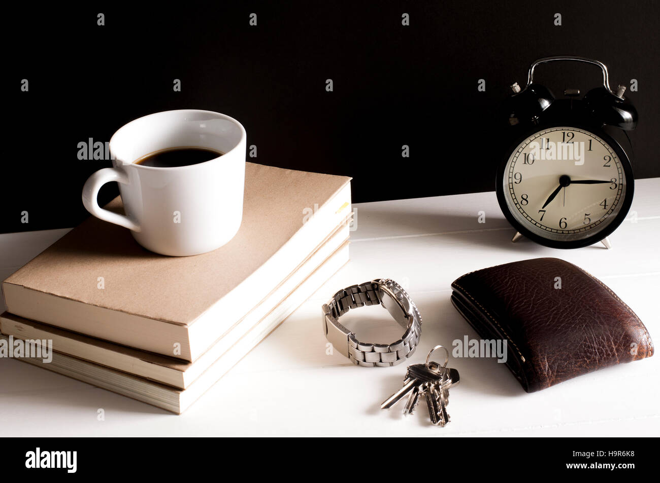 Wallet,regarder et porte-clés à côté d'une tasse de café sur le dessus les livres et rétro réveil sur tableau blanc en face de grunge fond noir. Banque D'Images