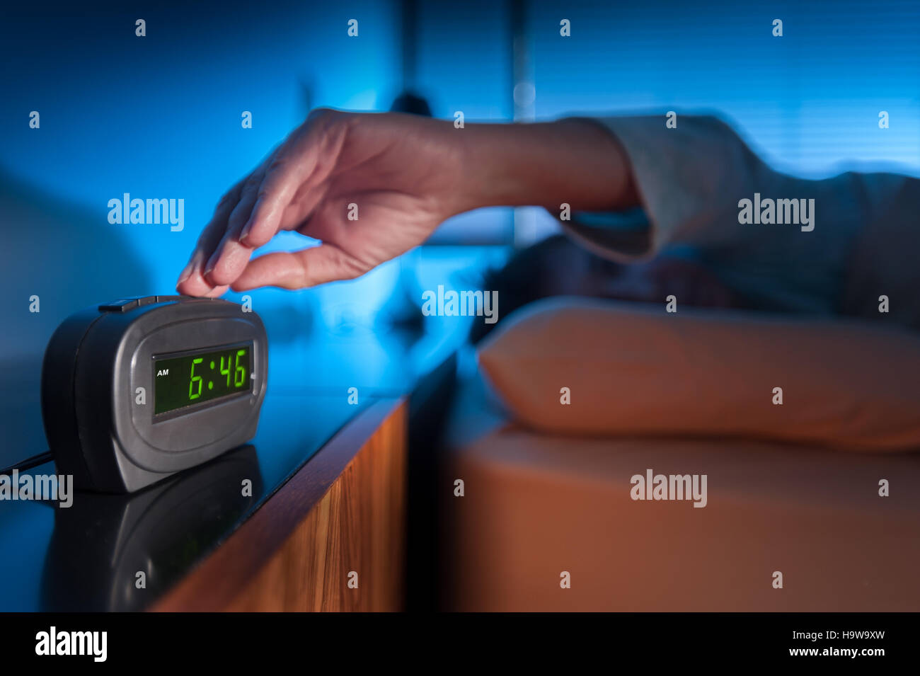 Femme en appuyant sur bouton snooze sur digital réveil tôt le matin Banque D'Images