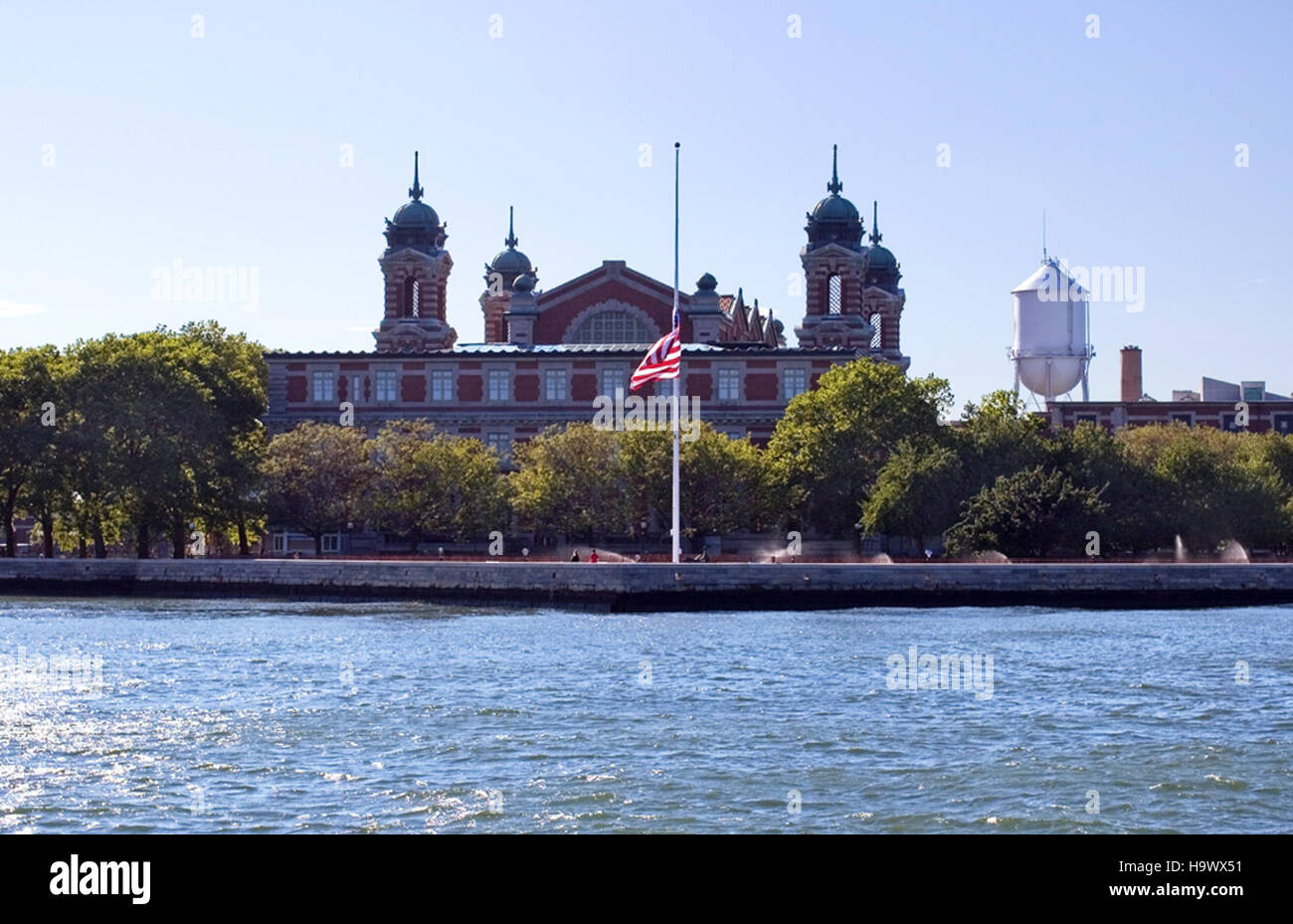Un drapeau américain flotte à mi-bâton sur Ellis Island, symbolisant le souvenir national. Ellis Island, un monument historique, a servi de porte d'entrée à des millions d'immigrants arrivant aux États-Unis à la fin du XIXe siècle et au début du XXe siècle. Banque D'Images