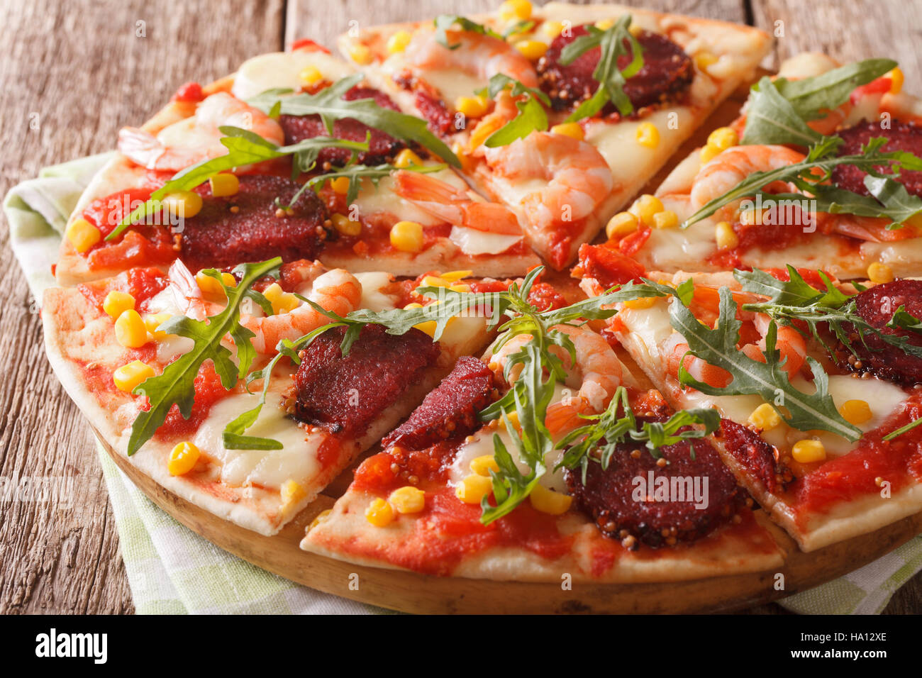 Pizza aux crevettes, salami, fromage et roquette close-up sur une planche de bois horizontal. Banque D'Images
