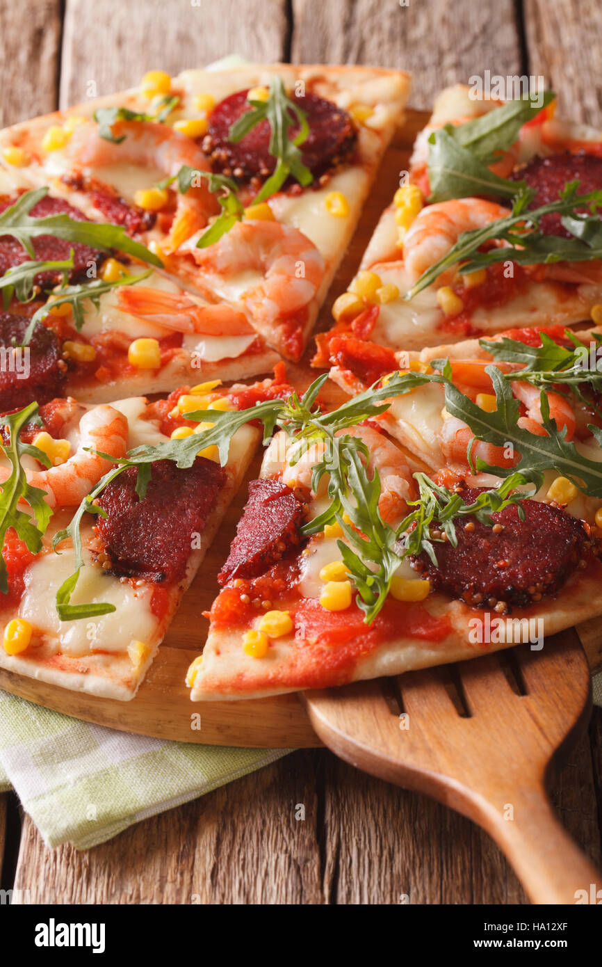 Tranches de pizza aux crevettes, salami, fromage et roquette close-up sur une planche de bois. La verticale Banque D'Images