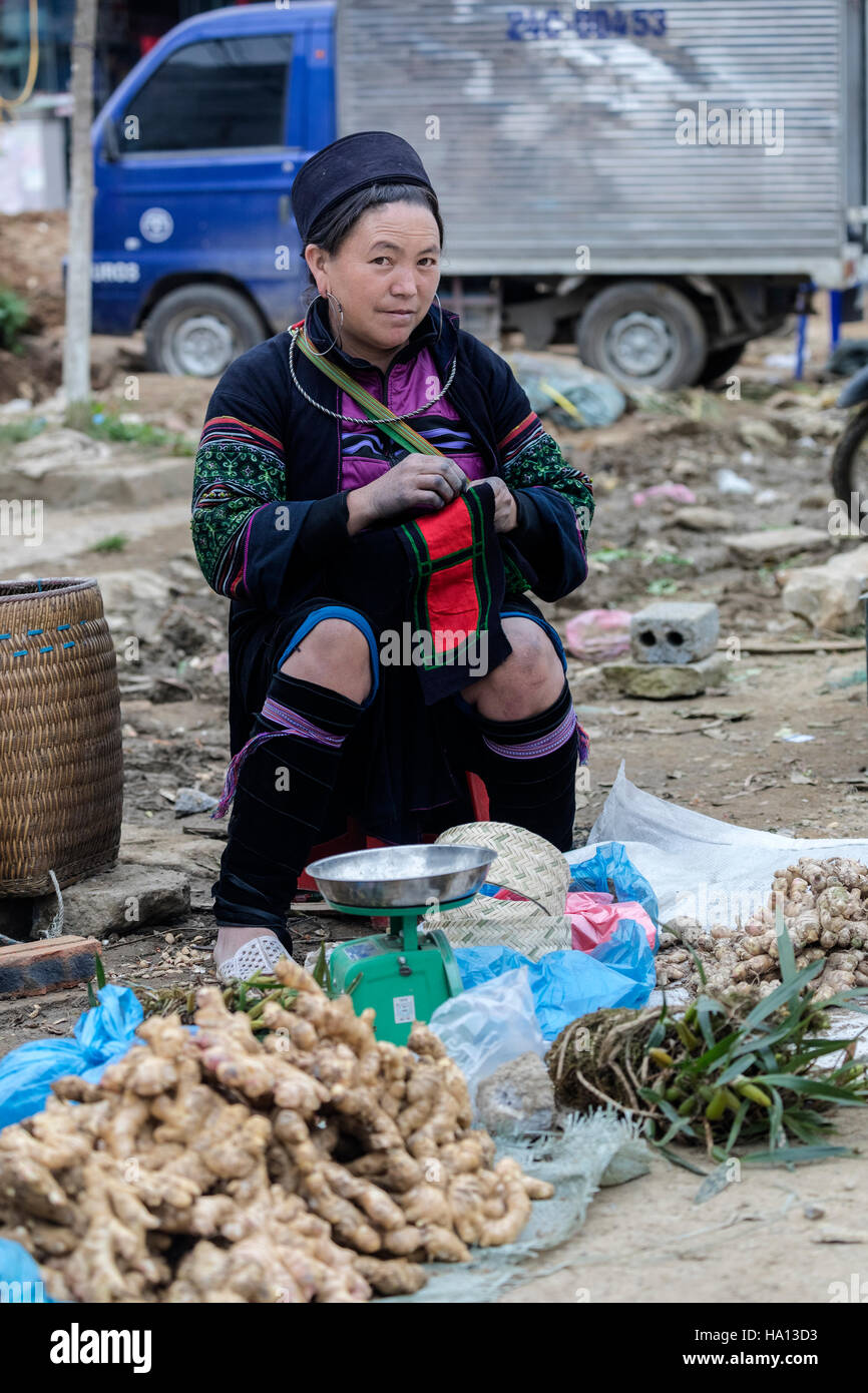 Couture femme Hmong noir lors de l'attente pour les clients et la vente de gingembre sur le marché local dans la région de Sapa, Vietnam, Asie Banque D'Images