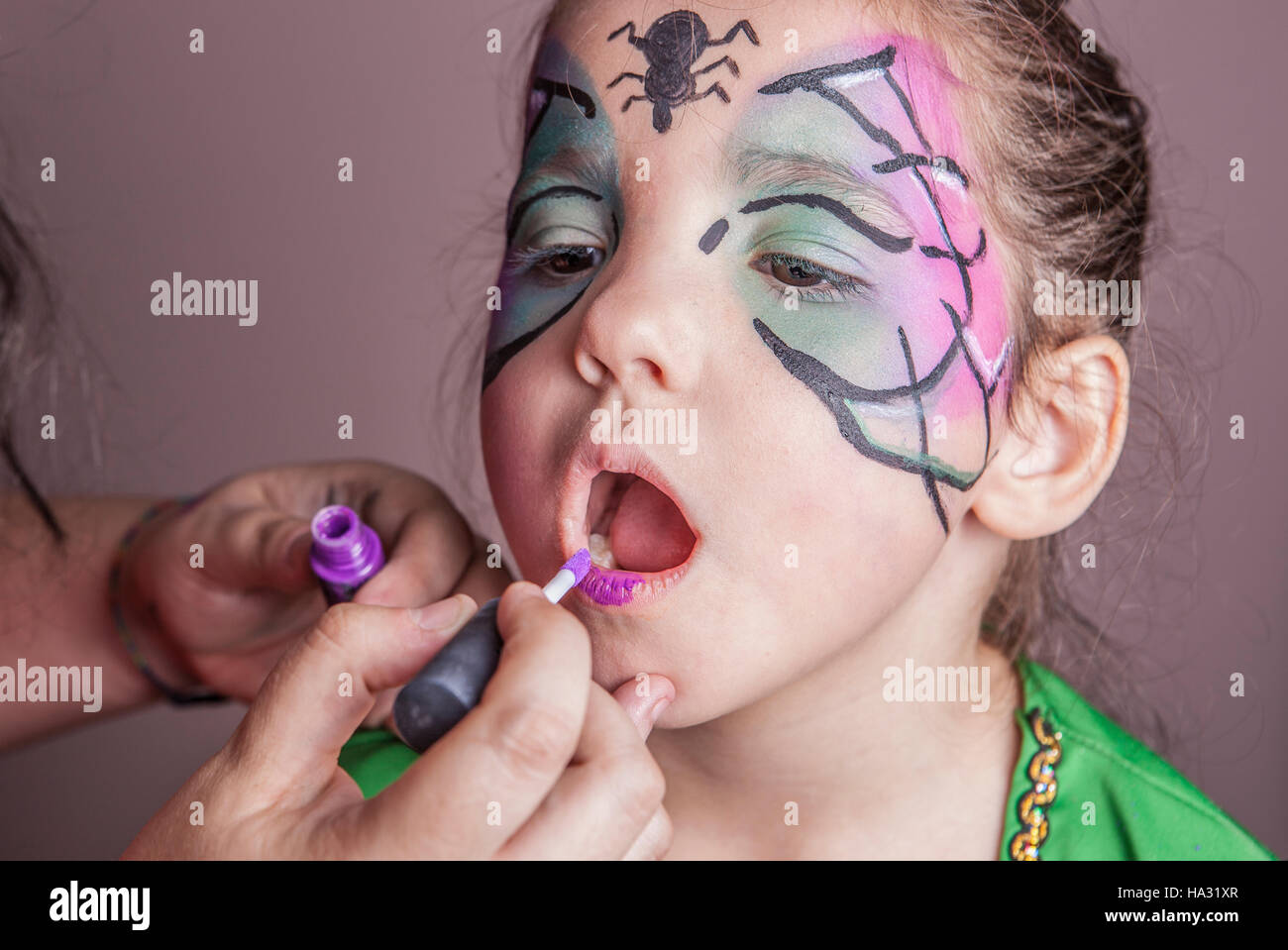Make-up artiste travaillant avec une petite fille avant Halloween party. Elle est l'application de rouge à lèvres violet Banque D'Images
