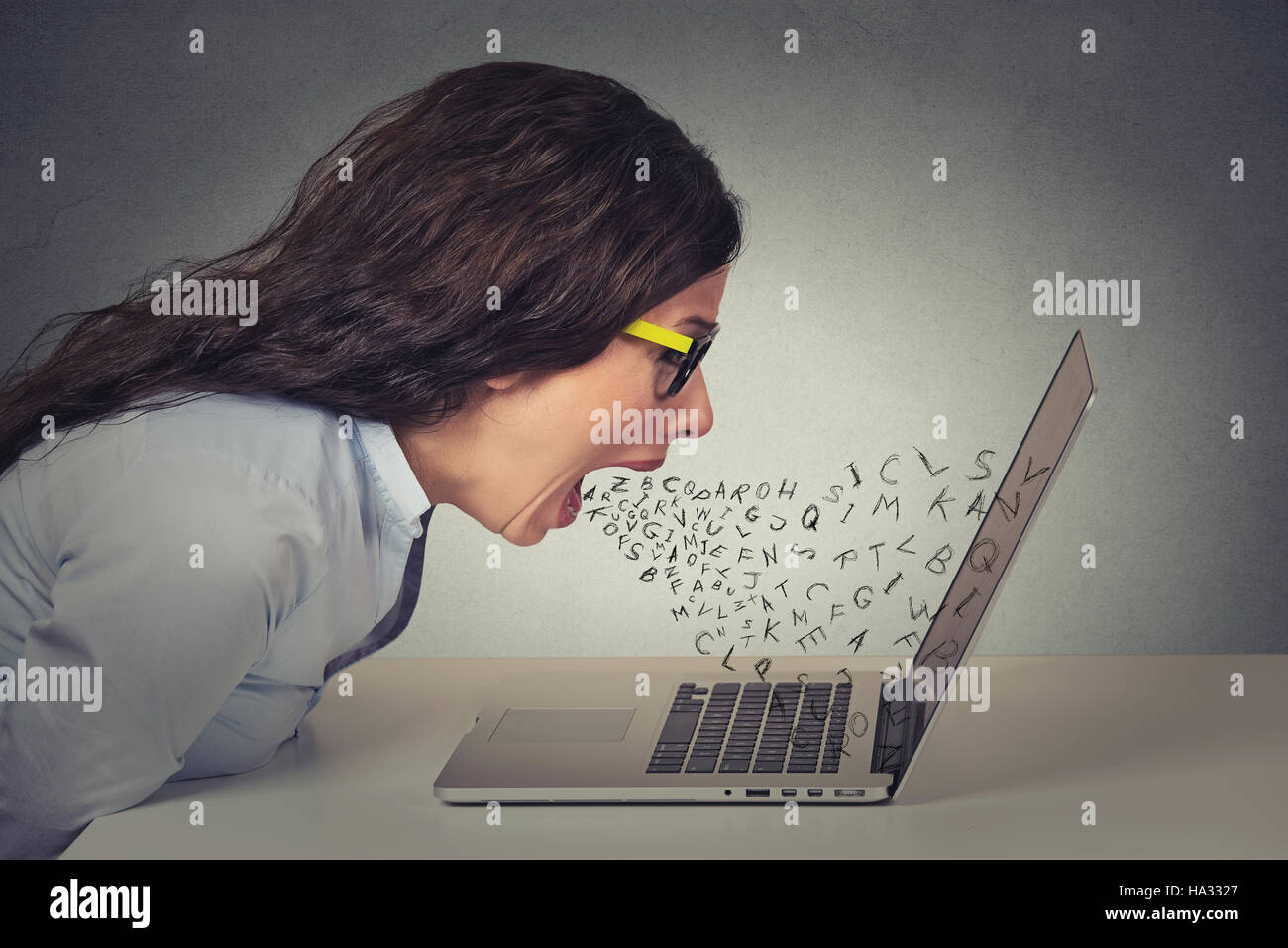 Furieuse colère businesswoman working on computer, hurlant de lettre de l'alphabet qui sortent de la bouche ouverte. Des émotions négatives, les expressions du visage, Banque D'Images