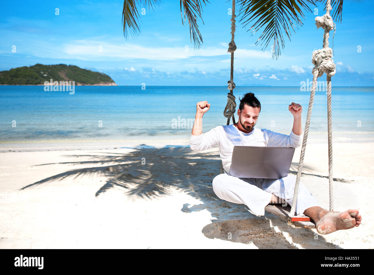 Businessman wearing white offres sitting on beach swing avec coffre Banque D'Images