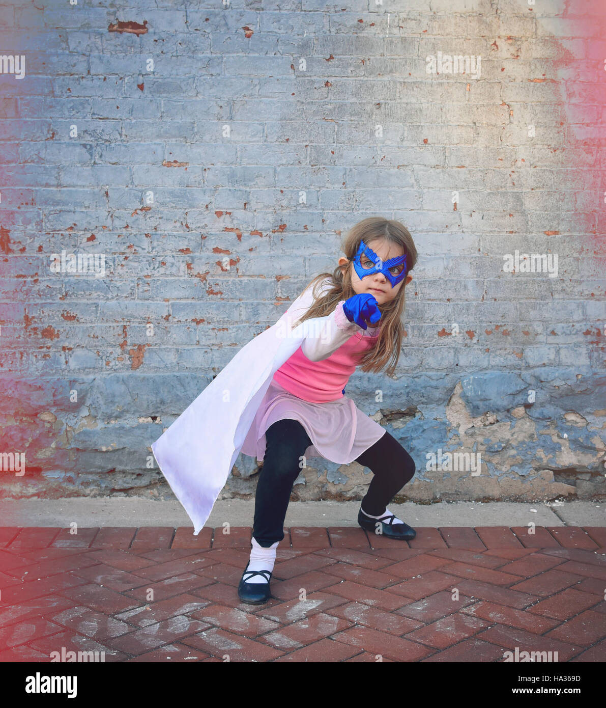 Un peu de super héros enfant est debout à l'extérieur contre un vieux millésime mur de brique pour une éducation ou concept créatif. Banque D'Images