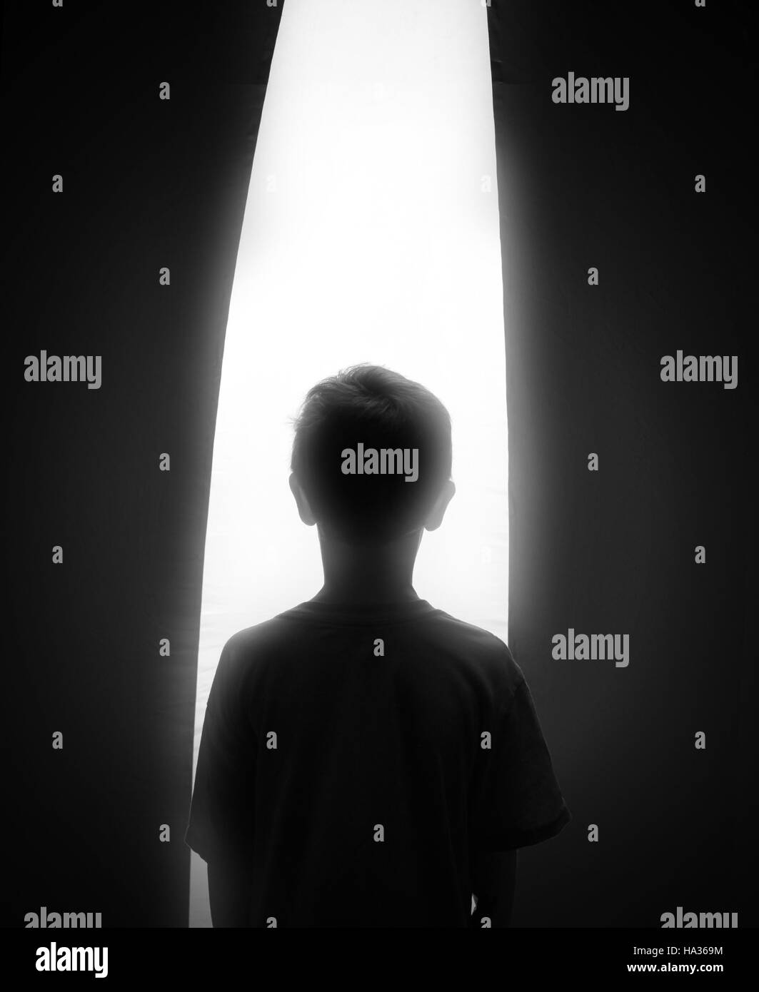 Une silhouette en noir et blanc d'un jeune garçon à la recherche d'une fenêtre d'un blanc brillant espoir, rêve ou foi concept. Banque D'Images