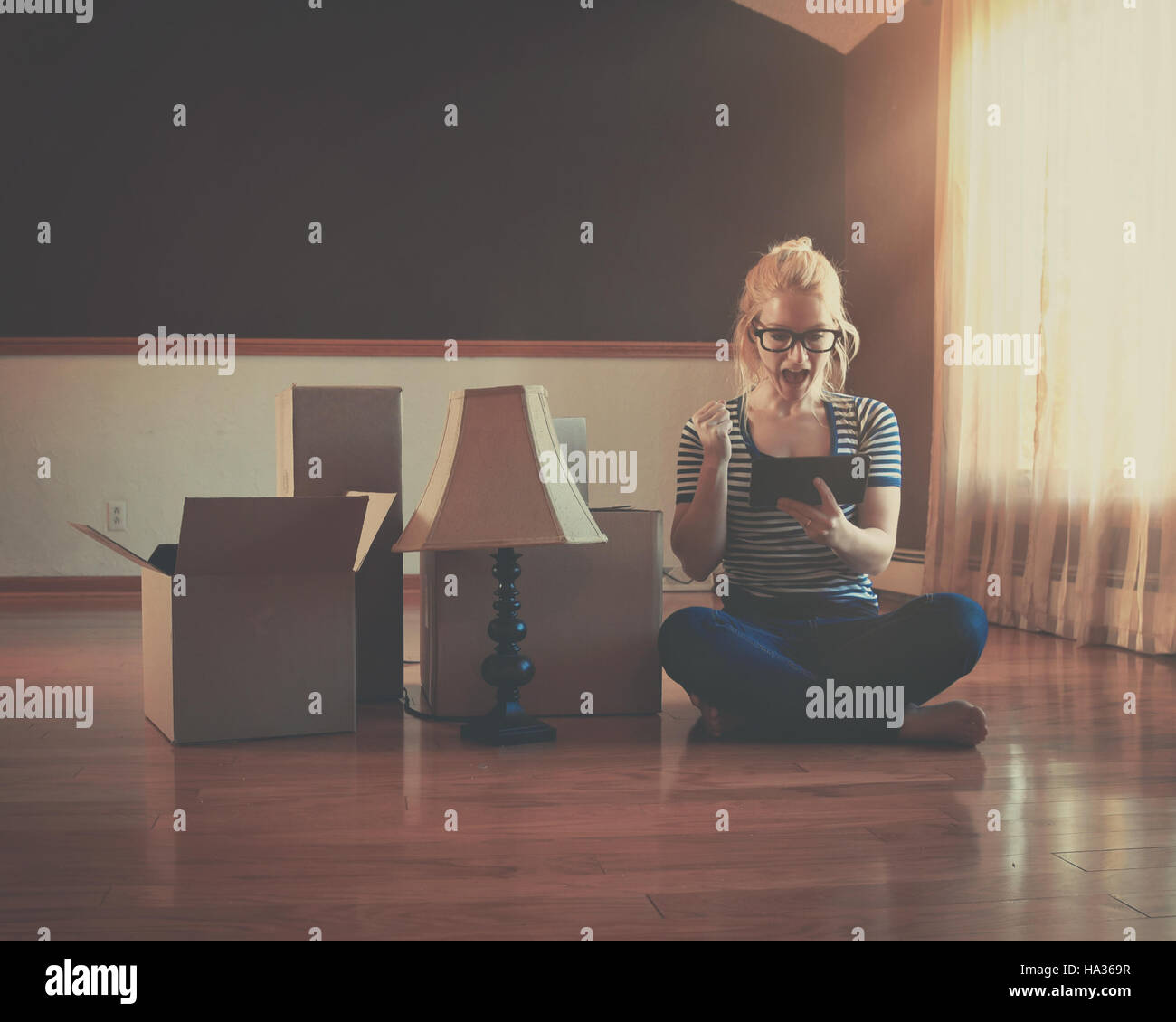 Une fille est assise dans une salle vide avec des cases. Elle est maintenant une technologie tablette pour un déménagement ou de design d'intérieur concept. Banque D'Images