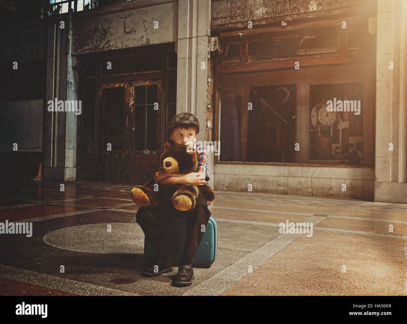 Peur d'un jeune garçon est assis sur une valise de voyage dans un vieux bâtiment holding a teddy bear pour un concept de sécurité ou la solitude Banque D'Images
