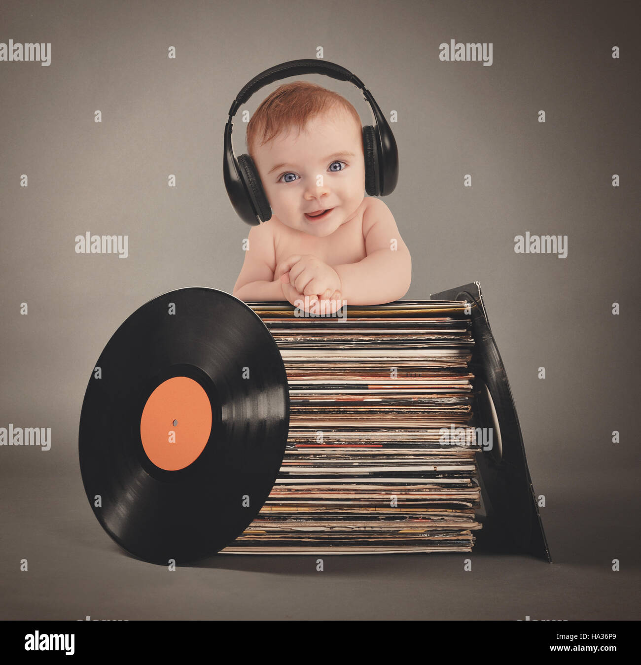 Un petit bébé porte des écouteurs de musique rétro avec les disques vinyles sur un fond gris pour un parti ou divertissement concept. Banque D'Images