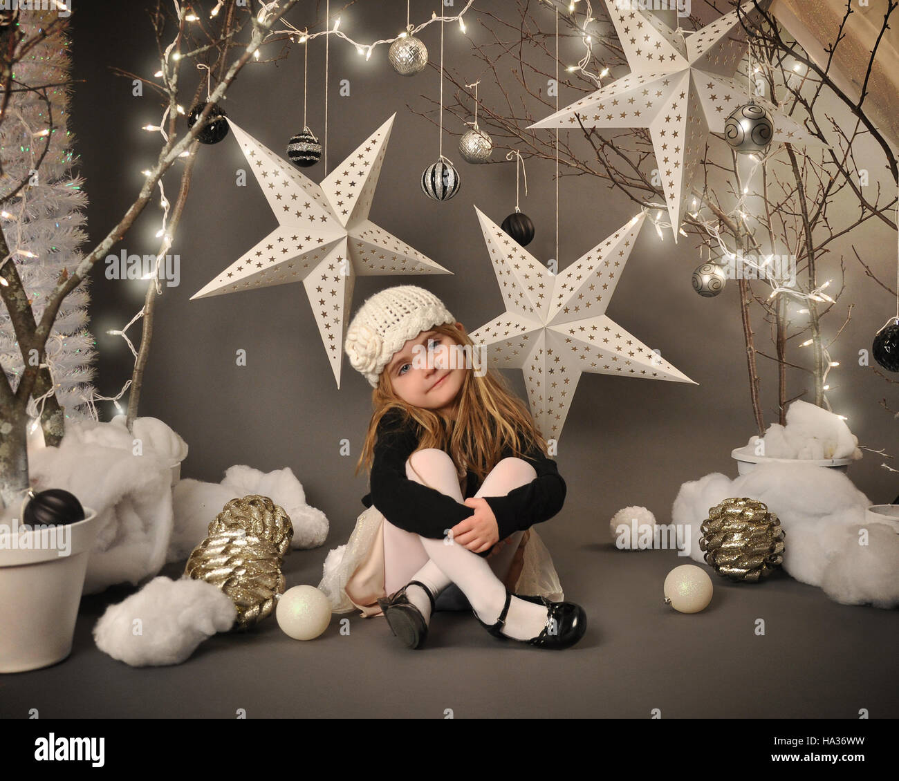 Une petite fille est assise dans une féerie d'hiver setip avec arbres, pendaison des étoiles et les lumières de Noël autour de l'arrière-plan pour une saison ou maison de con Banque D'Images