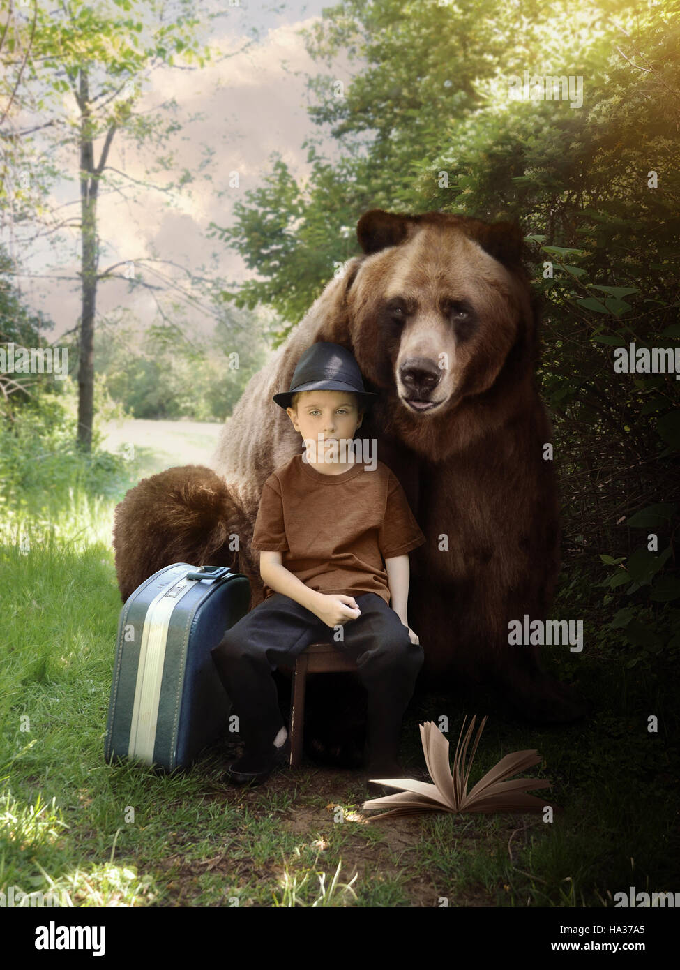 Un jeune garçon est assis sur un sentier dans les bois avec une valise et livre avec un ours animal derrière lui pour un voyage imaginaire ou le concept. Banque D'Images