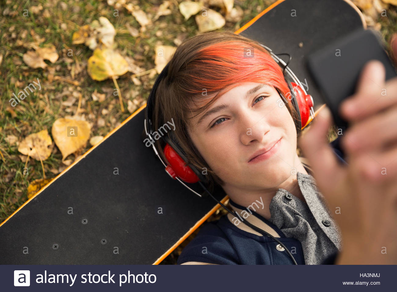 Vue aérienne du garçon aux cheveux teints en rouge portant sur planche à l'aide de téléphone cellulaire dans les feuilles d'automne Banque D'Images