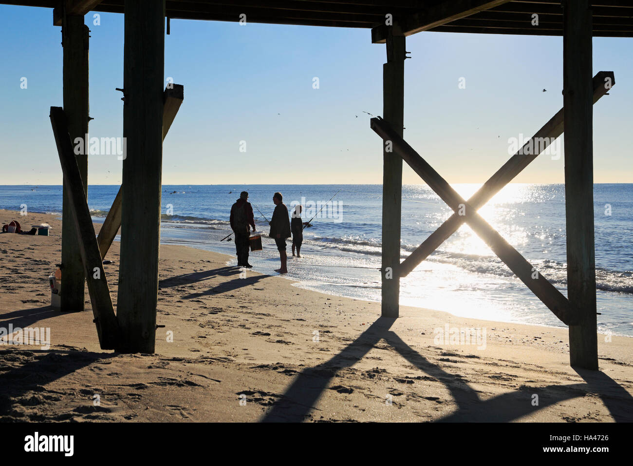 Silhouette de pêcheurs sur la plage, dans la lumière du matin, encadré par pier. Plage de l'Atlantique, de la Caroline du Nord. Banque D'Images