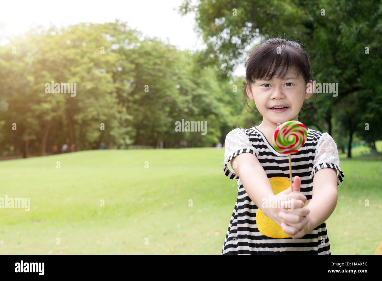 Asian little girl eating lollipop extérieur dans spring park Banque D'Images