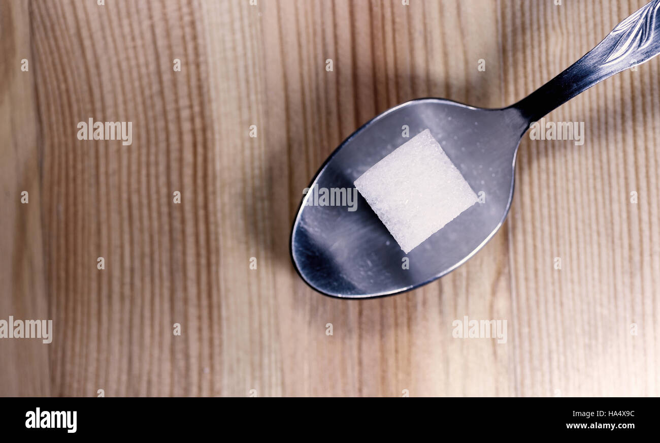 Cube de sucre simple paiement reposant sur une cuillère de métal de l'argent sur un bureau en bois cuisine texturés. Passage horizontal image. Banque D'Images