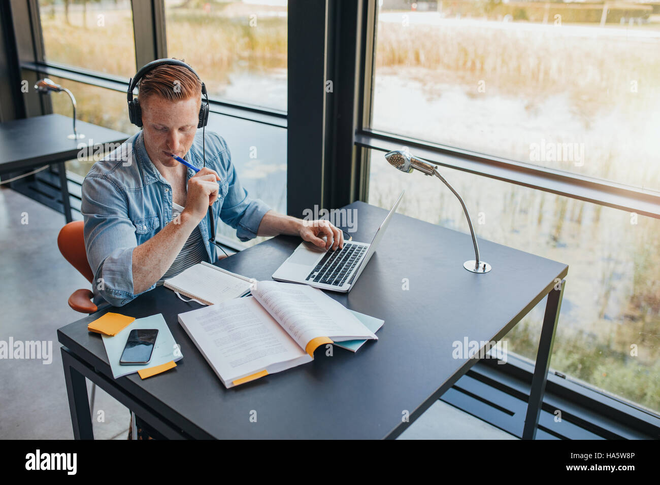 Shot of young male student la préparation de travail scolaire en bibliothèque. Man reading book at college library. Banque D'Images
