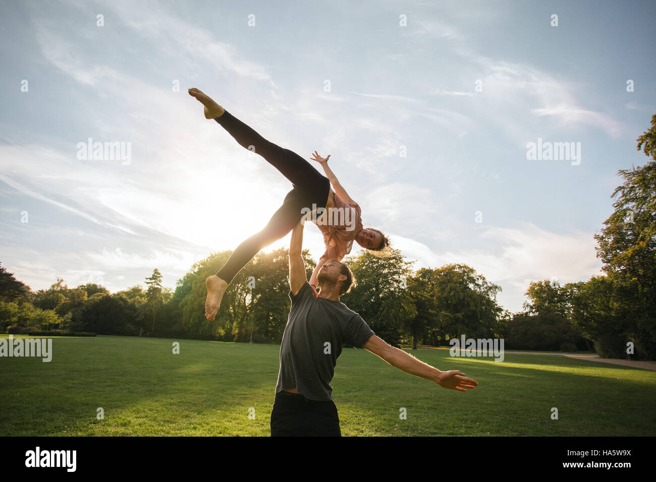 L'homme et de la femme faisant paire yoga piscine dans un parc. Fit young couple practicing acroyoga. L'homme et femme d'équilibrage de levage sur un côté. Banque D'Images