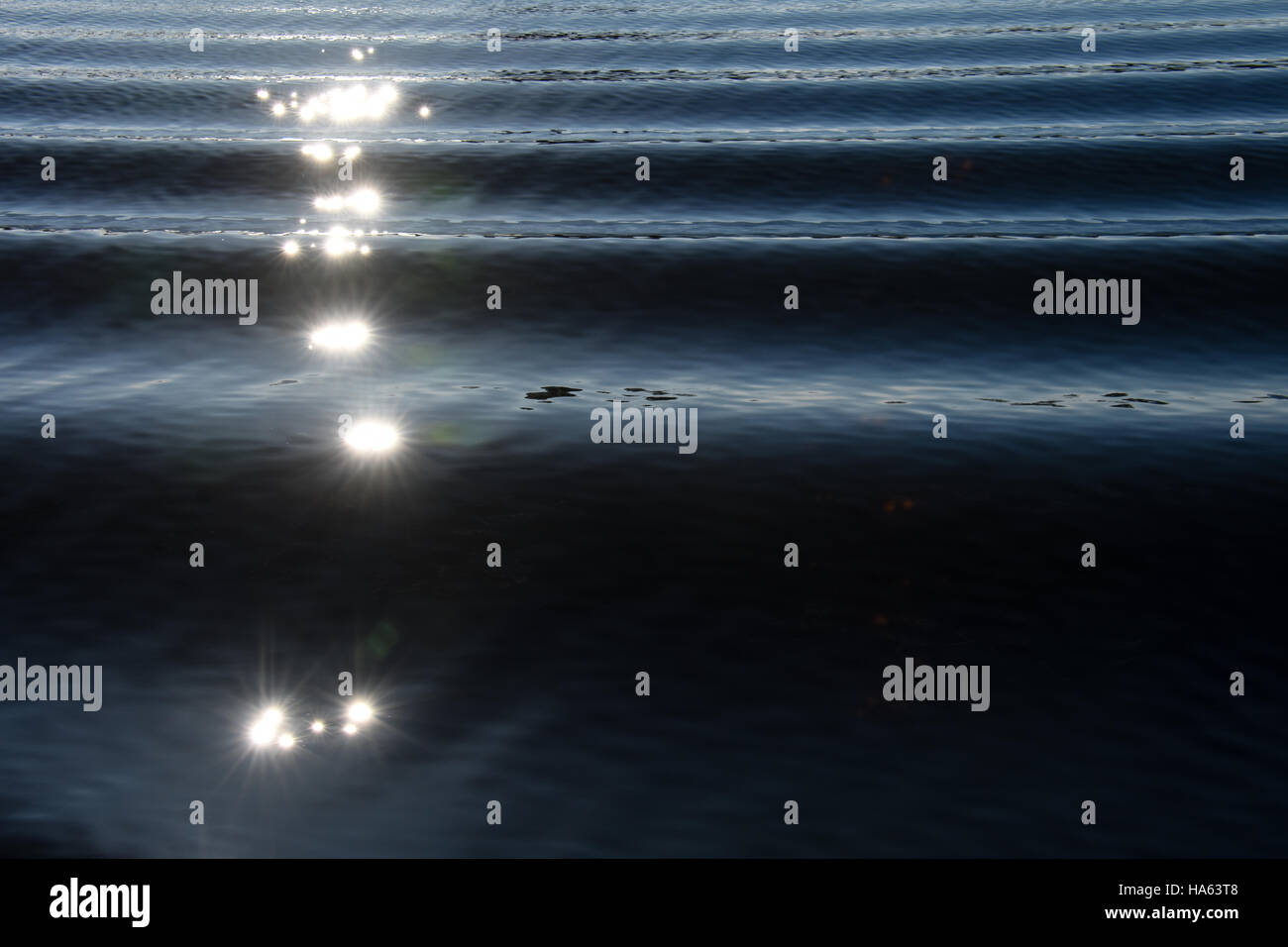 La lumière du soleil en étoile sur le bateau service créant un motif intéressant de vagues sur l'eau ridée bleu. Banque D'Images